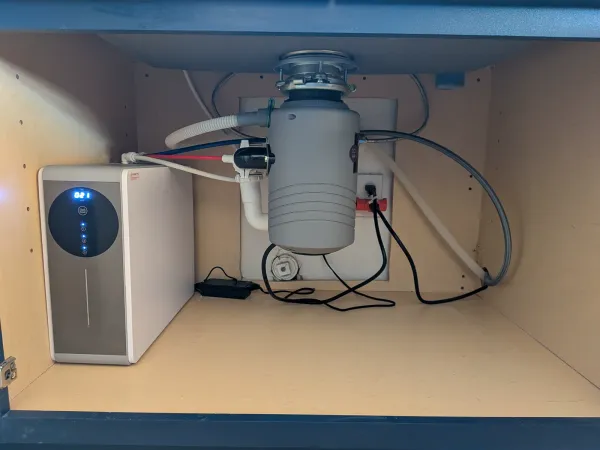 Finished under-sink view showing the installed garbage disposal, RO system, drain piping, and water lines